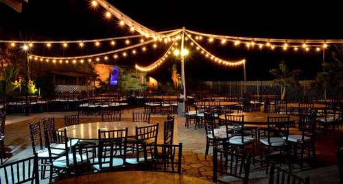 A group of tables and chairs under string lights  Description automatically generated